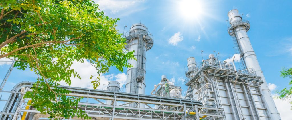 An industrial plant with green foliage in the foreground under a blue sky